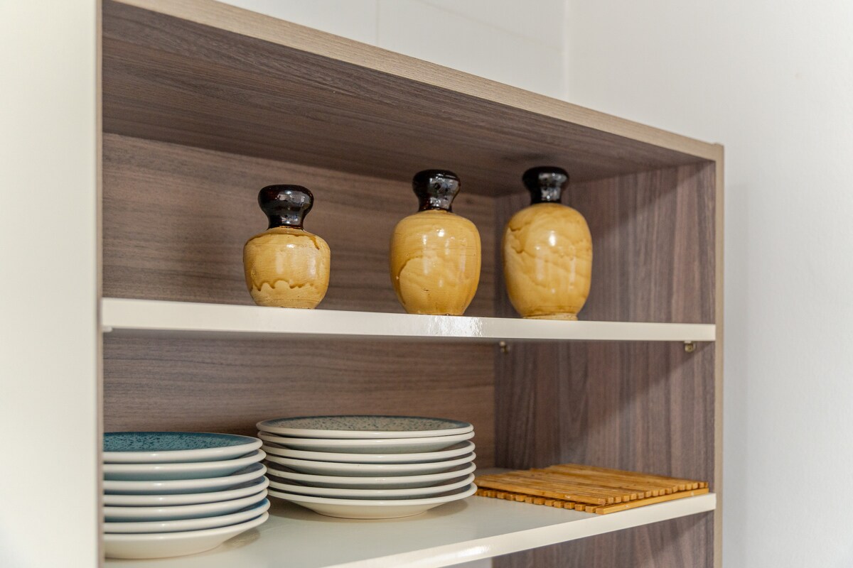 A modern shelving unit displays an assortment of tableware, including stacked plates and decorative ceramic jars. The clean lines and neutral tones of the shelving complement the organized arrangement of items.