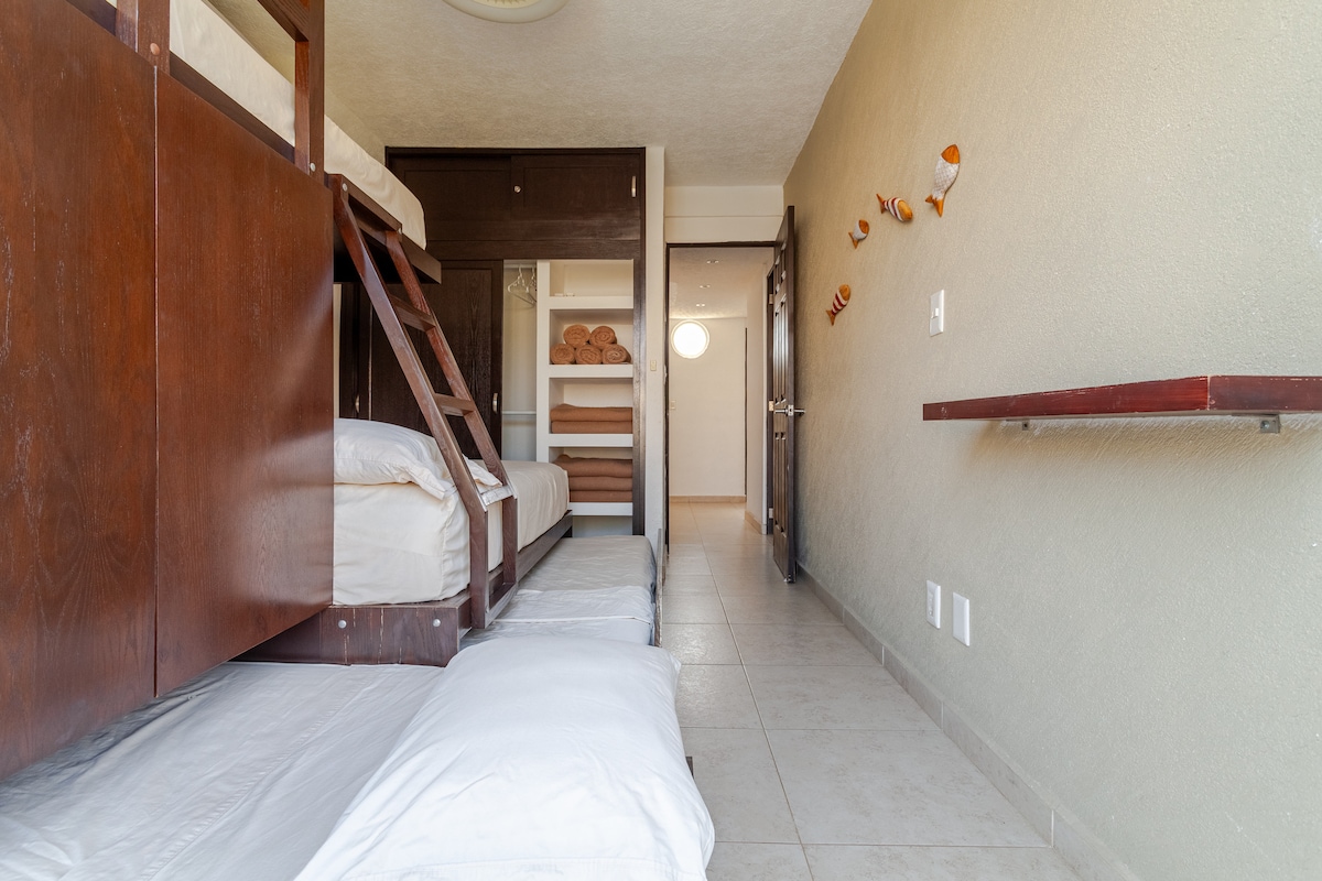 Recámara con 3 camas individuales y una matrimonial. Closet. Terraza privada con vista a las áreas verdes y albercas. Aire acondicionado y ventilador.