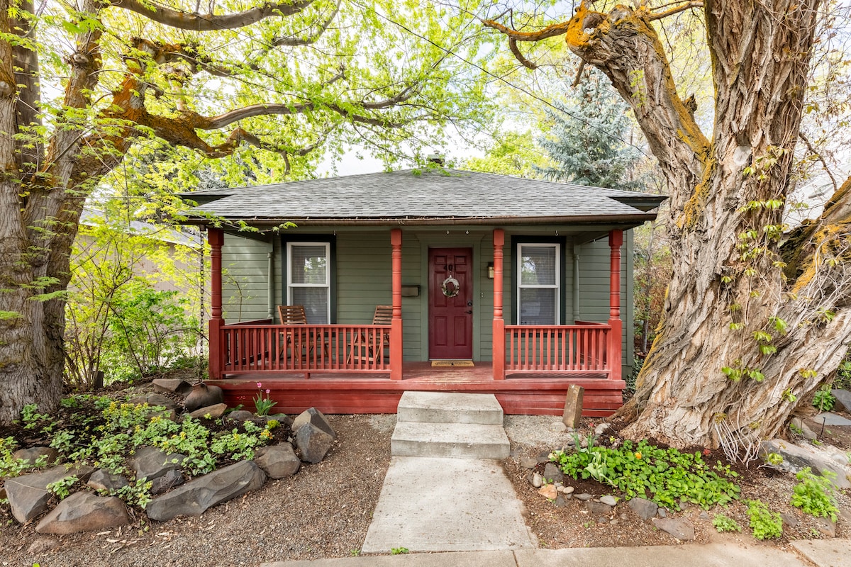 A charming house exterior features a welcoming front porch with two chairs and a decorative wreath on the door. Lush greenery surrounds the home, with mature trees providing shade and landscaping that adds to the inviting curb appeal.