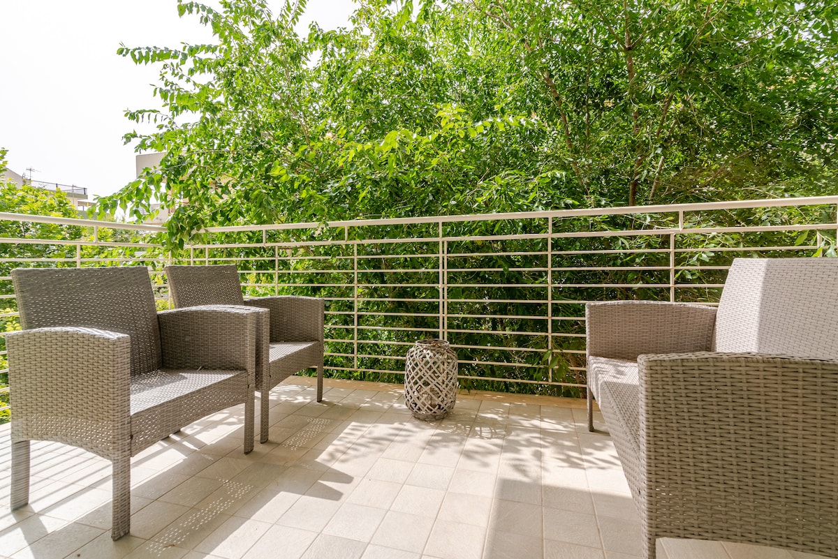A private terrace is presented with two comfortable armchairs facing vibrant greenery. A decorative lantern adds a subtle accent to the space, while a tiled flooring ensures a clean and inviting atmosphere.