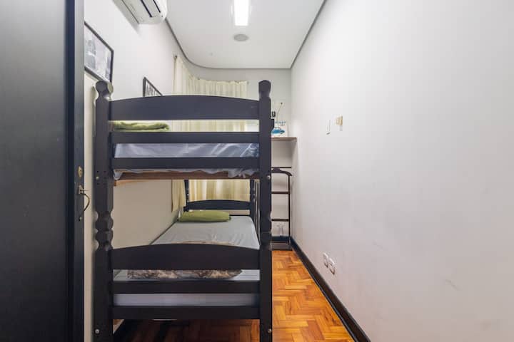 Habitación pequeña con litera, estante, aire acondicionado frío y caliente y baño enfrente. Ropa de cama y mantas 