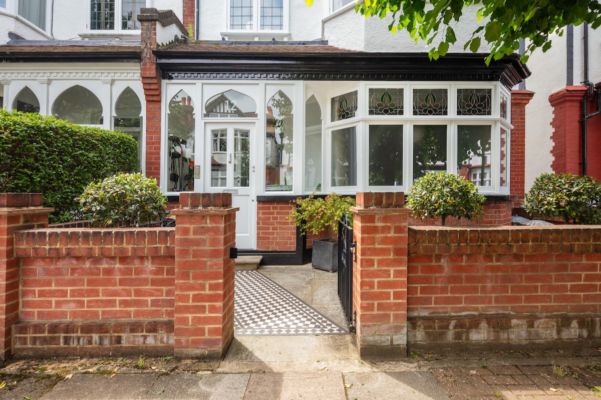 A welcoming entrance features a brick wall with neatly trimmed hedges on either side. A decorative walkway leads to a white door framed by large, glass-paneled windows. Arched windows enhance the inviting front porch, creating a bright and airy entryway.