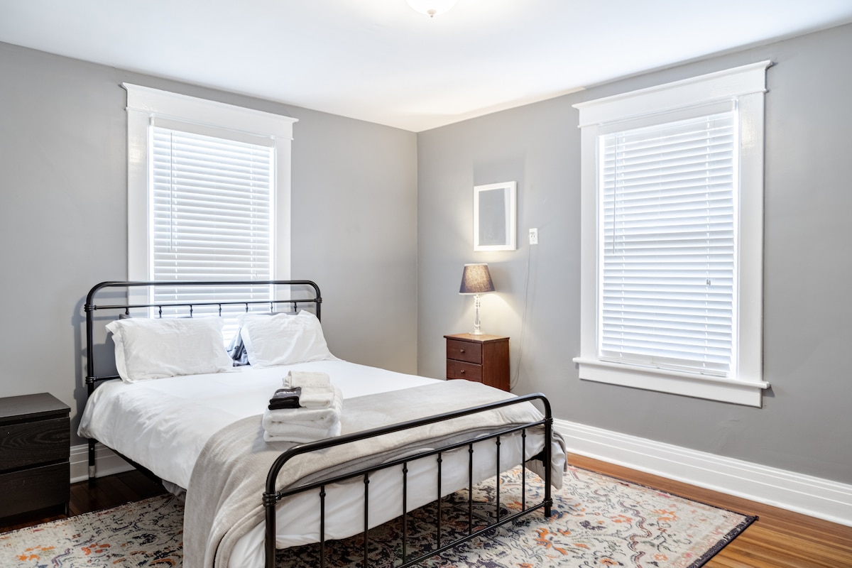 这间宁静的卧室配有一张时尚的黑色金属床，配有清爽的白色床上用品，让您安心入睡。 带有白色装饰的大窗户带来光线，而柔软的灰色墙壁营造出宁静的感觉。 带台灯的床头柜为房客增添了温暖和功能！