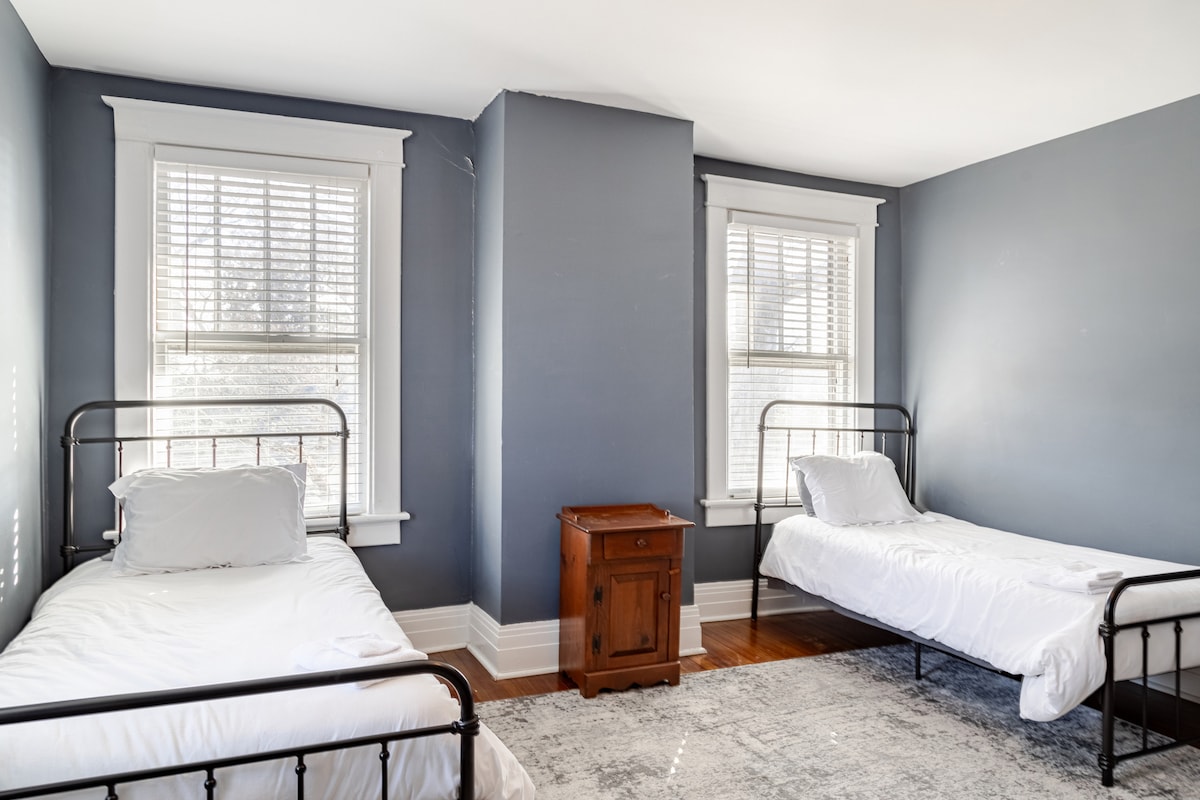 这间舒适的房间专为儿童设计，配有两张带黑色金属框架的单人床，让您安心入住。 柔软的蓝灰色墙壁和大窗户照亮了空间。 木质床头柜增添了魅力，而毛绒地毯为小脚提供了温暖。