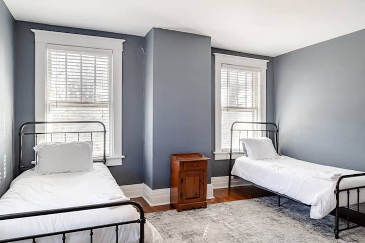 Diseñada para niños en mente, esta acogedora habitación tiene dos camas individuales con marcos de metal negro para una estadía tranquila. Las suaves paredes de color azul grisáceo y los grandes ventanales iluminan el espacio. Una mesita de noche de madera agrega encanto, mientras que una lujosa alfombra proporciona calidez para los pies pequeños.