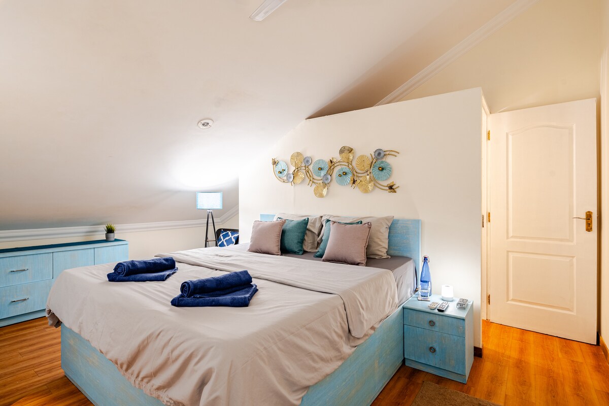 The Bedroom with ensuite bathroom located on the upper level of this 1BHK Duplex Apartment. Veliki bračni krevet s noćnim ormarićima, svjetlima i punktovima za punjenje. Jedan kauč na razvlačenje u kutu za taj dodatni prostor. 