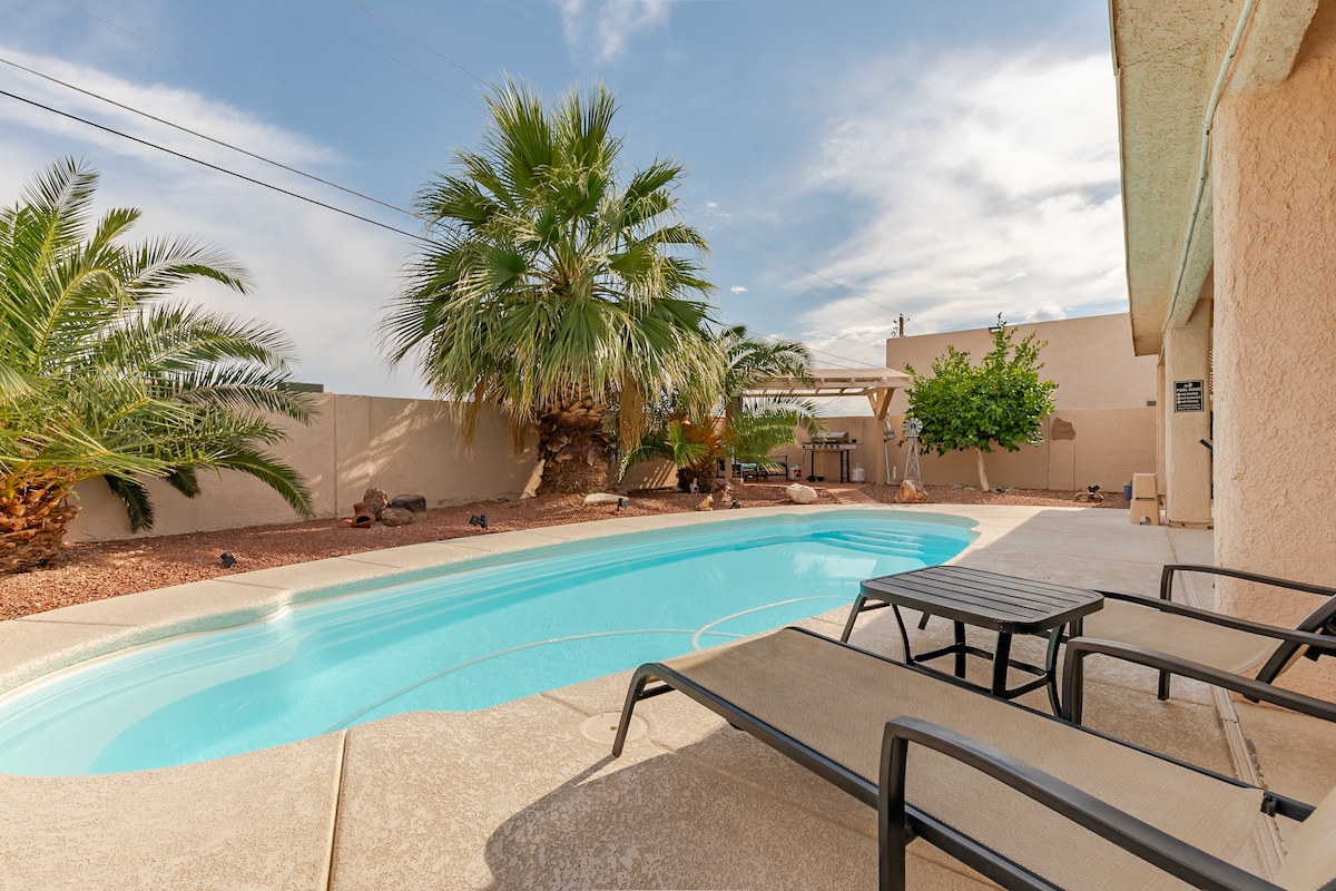 A private pool area is showcased with a clear blue swimming pool surrounded by a sun deck. Two lounge chairs are positioned beside the water. Lush palm trees and desert landscaping provide a tropical ambiance, creating a serene outdoor space for relaxation.