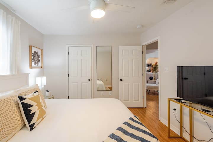 Dormitorio de invitados con una cómoda cama tamaño king, televisor inteligente y espejo grande, lo que crea un refugio acogedor para relajarse. Ideal para huéspedes que buscan comodidad y estilo después de un día en Navarre Beach, esta habitación trae el encanto de la Costa del Golfo a cada detalle.