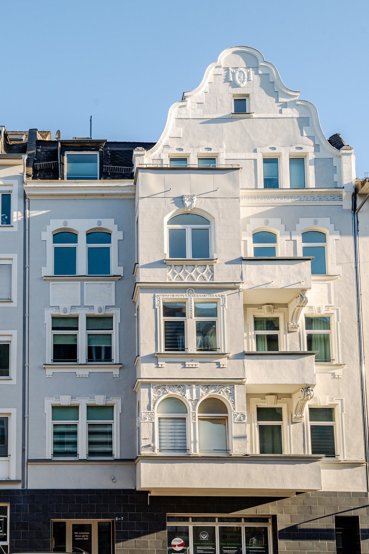 An elegant building facade features a blend of architectural styles, characterized by decorative elements and a symmetrical design. The structure showcases multiple windows with varying shapes, while the intricate detailing on the upper levels draws attention to the unique craftsmanship.