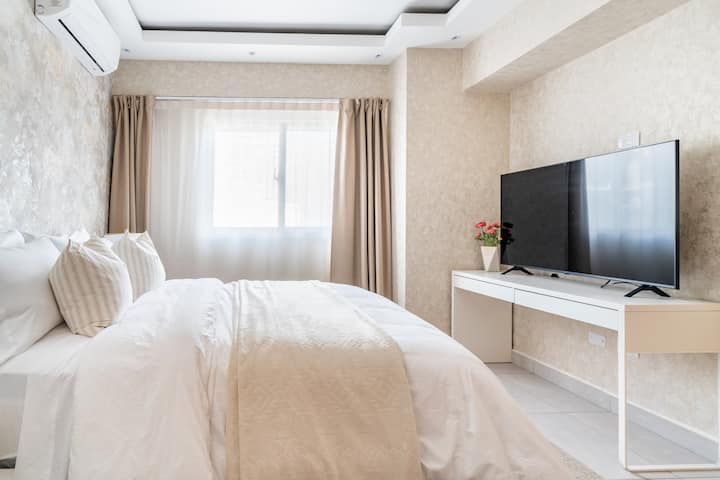 Pumzika katika chumba chenye nafasi kubwa chenye kitanda kikubwa, meza ya kando ya kitanda na televisheni ya inchi 55, inayotoa mwonekano wa mazingira ya nje.