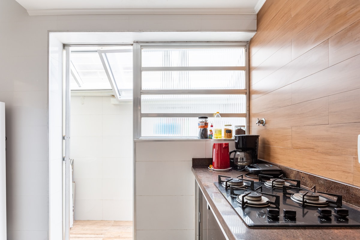 A practical kitchen space is displayed, featuring a gas stove with four burners. Natural light is let in through a window aligned with the countertop, enhancing the light-colored walls and wooden accents.