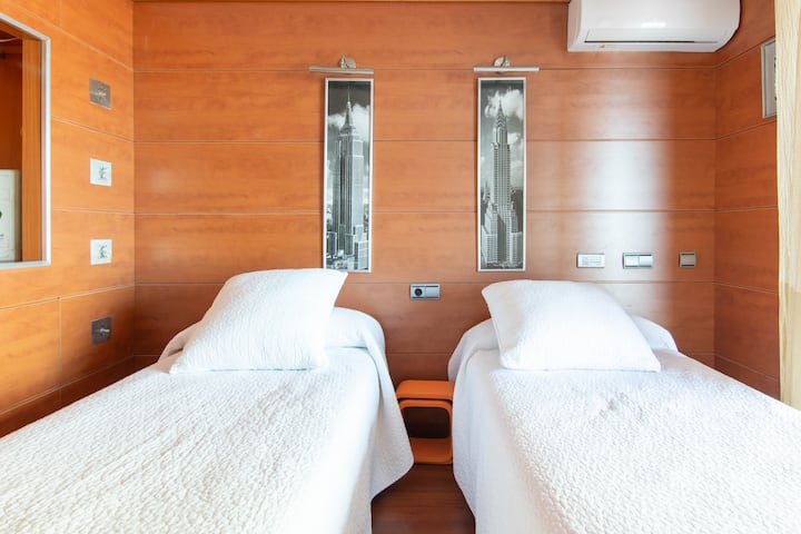 Spálňa s drevenými stenami a podlahou pozostávajúca z dvoch 90 cm lôžok, samozrejme s výhľadom na pláž 