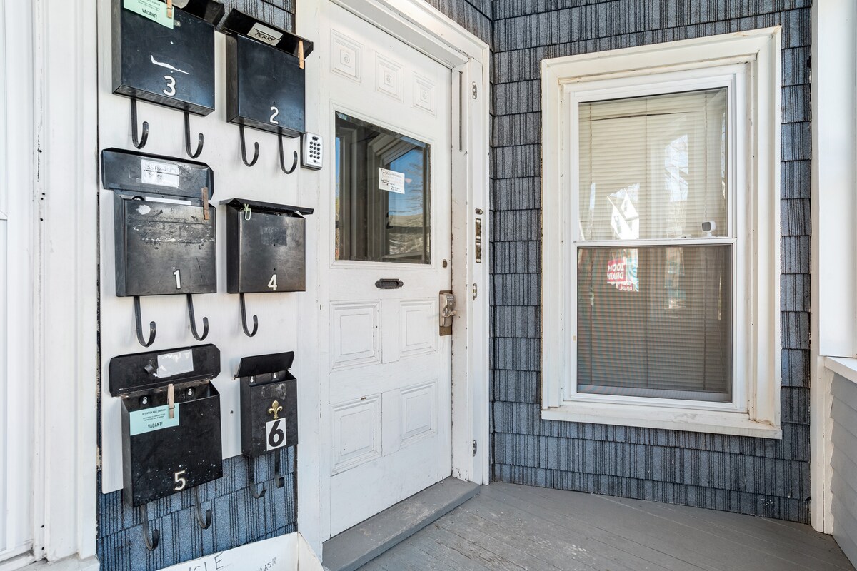 The entrance area features a white door with a vintage design, positioned next to a row of six black mailboxes mounted on the wall. A large window is visible, allowing natural light to illuminate the entryway.