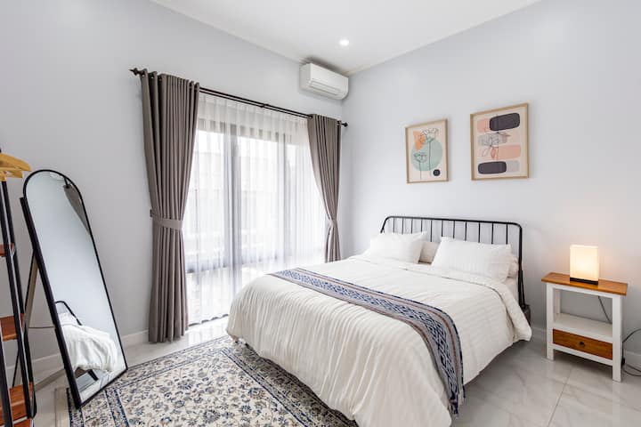 חדר שינה עם מיטת קווין סייז ומתקני מיזוג אוויר. המיקום למעלה ויש חלונות גדולים הפונים לגינה הקדמית ולרחוב.