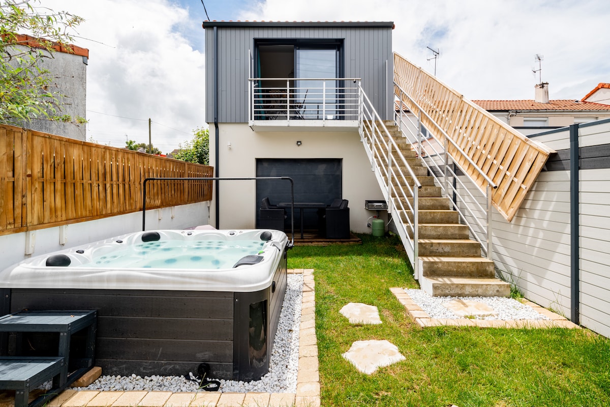 A private garden features a spacious jacuzzi surrounded by landscaping. The jacuzzi is adjacent to a contemporary house that includes a flight of stairs leading to an upper level. A seating area can be seen nearby, providing a tranquil outdoor environment.