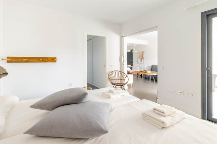 Quarto iluminado e arejado com lençóis brancos frescos, travesseiros cinza macios e acesso direto ao terraço. O espaço se conecta à sala de estar através de uma elegante porta de celeiro e tem seu próprio corredor privado com armários dedicados e um banheiro.
