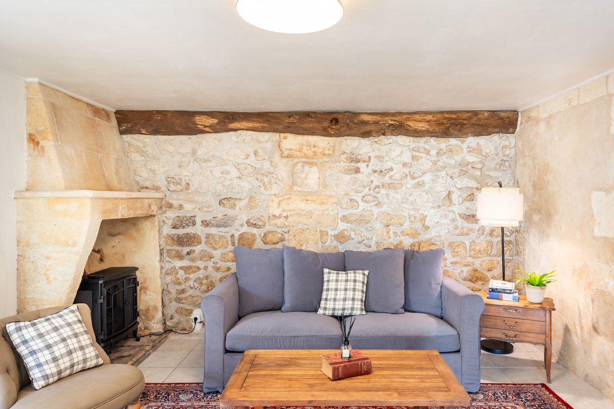 A cozy living area features a soft blue couch adorned with a checkered cushion, complemented by a wooden coffee table. A classic stone wall and a rustic wooden beam add warmth, while a stylish lamp provides ambient light next to a small plant on the side table.