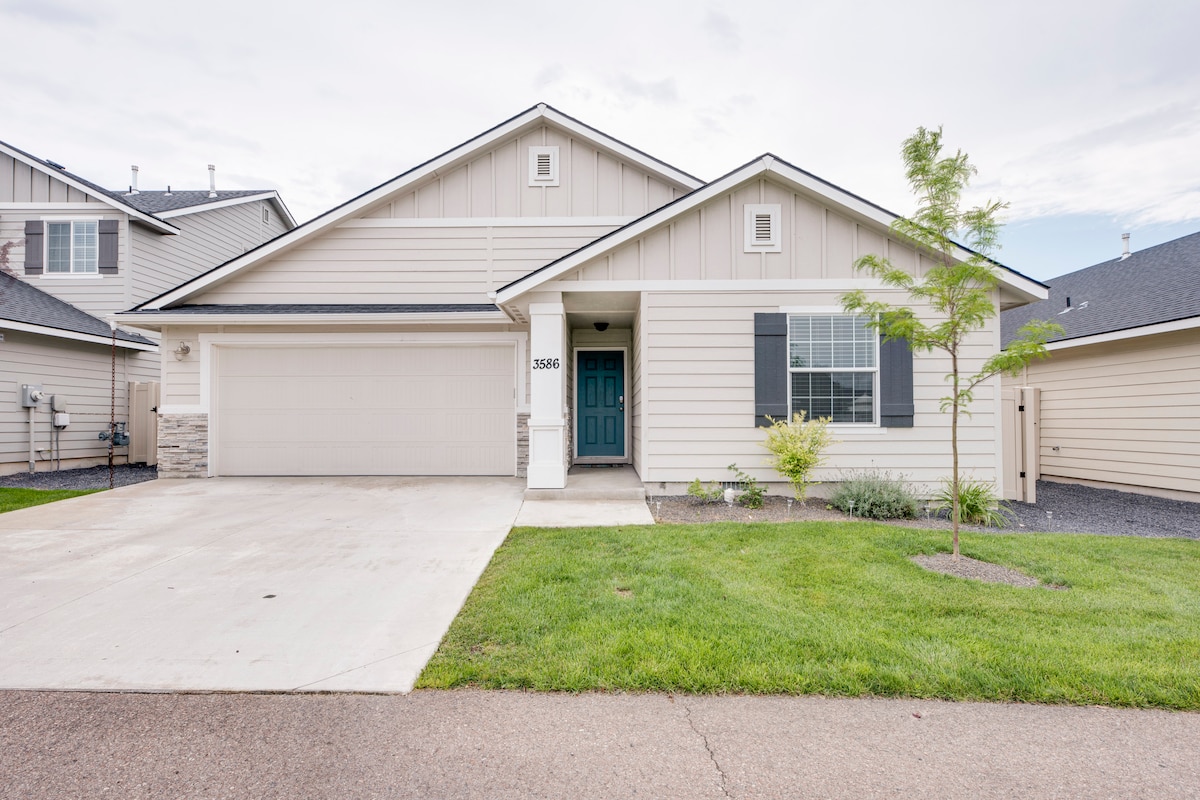 A modern single-story house is presented with a light-colored exterior and a contrasting dark front door. A neat lawn is maintained in front, along with a driveway leading to an attached garage. Minimal landscaping features are positioned alongside the pathway.