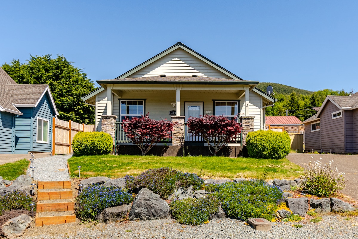 A charming single-story home features a welcoming front porch framed by vibrant bushes and neatly trimmed hedges. Gravel pathways lead to the entrance, while landscaped areas with colorful flowers and rock accents enhance the exterior. A peaceful neighborhood backdrop provides a beautiful view.