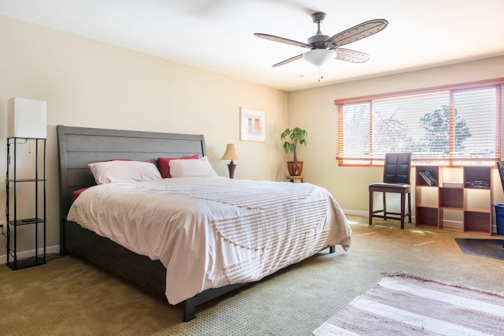 غرفة نوم كبيرة مع حمام مجاور ورفوف ملابس ومكتبين وتلفزيون. 