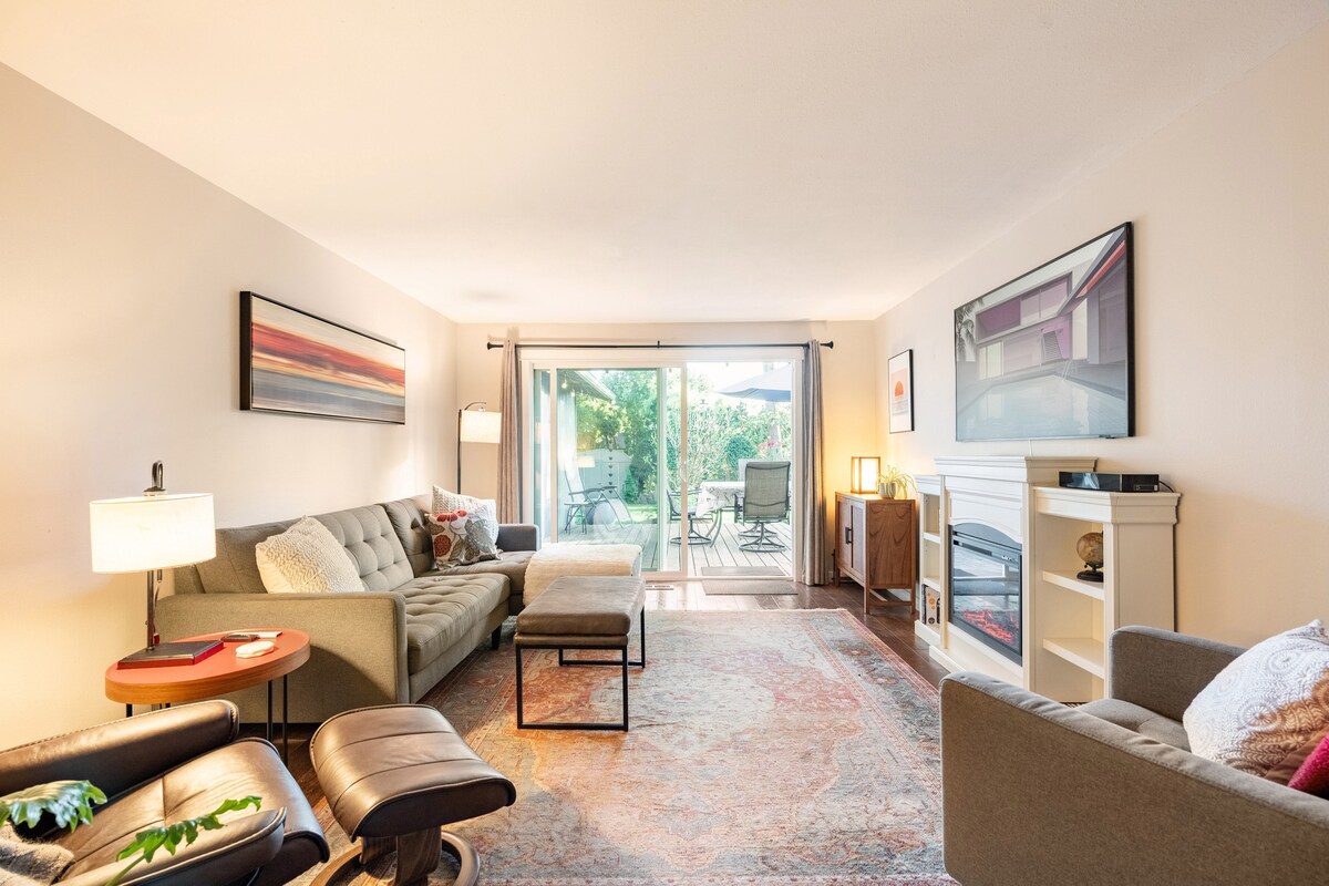 A well-furnished living area is present, featuring a soft gray sofa and a cozy armchair. A warm area rug lies underneath a coffee table. Large sliding glass doors lead to an outdoor space, allowing natural light to fill the room.