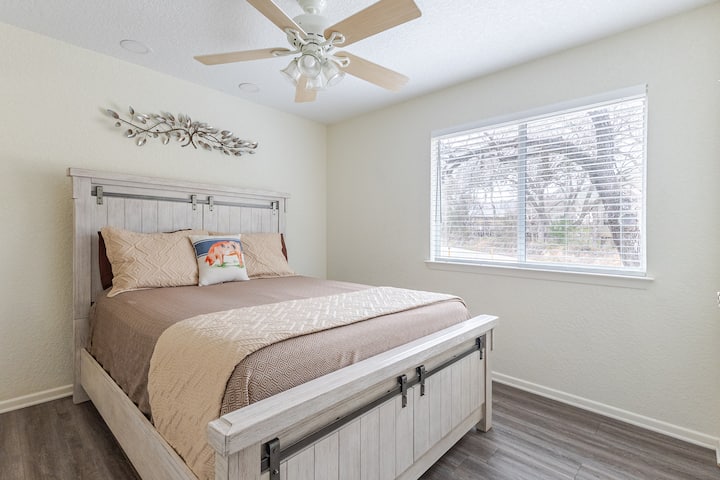 Comfortable bedroom with cozy bedding, ceiling fan, and natural light for restful nights after swimming, tubing, and exploring New Braunfels. Great for Spring Break getaways near the Guadalupe River and local hotspots.