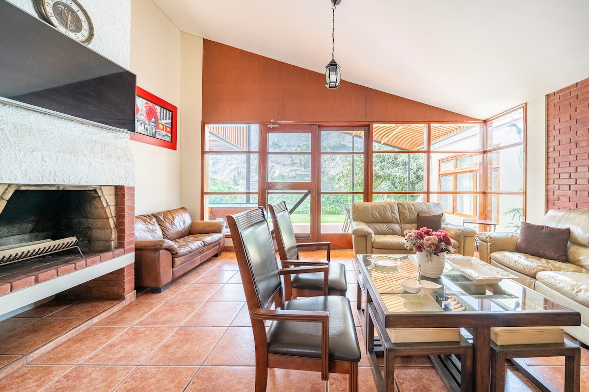 A spacious living area is highlighted by large windows that provide ample natural light and views of the outdoor landscape. Comfortable seating is arranged around a central coffee table, with a fireplace adding a touch of warmth to the room.