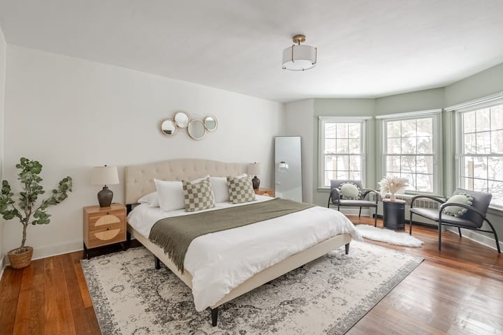 Sage King bedroom complete with a sitting area, TV, and a king Purple Mattress, organic cotton sheets, orthopedic pillows + feather pillows, and blackout blinds