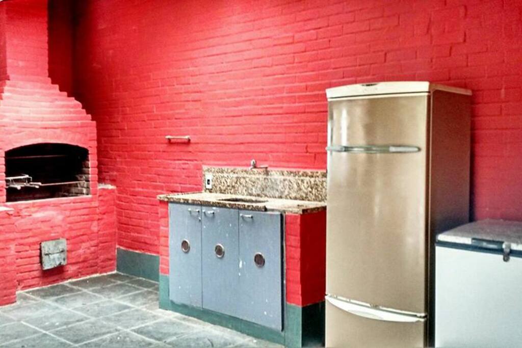 Espaço com churrasqueira com bancada e 3 geladeiras disponíveis.