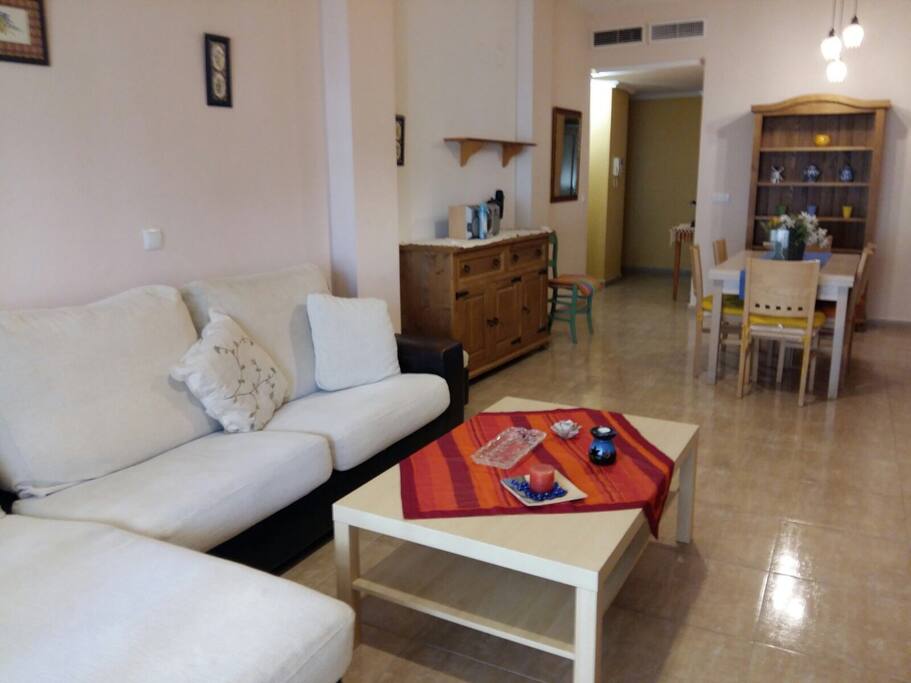 Amplio salón con balcón / terraza anexo. El cerramiento del balcón/terraza es doble, por lo que en el interior del salón la temperatura es muy estable todo el día. El salón dispone de sofá con chaise longue, una mesa centra y TV con TDT. También dispone de una mesa de comedor extensible y seis sillas así como muebles accesorios.