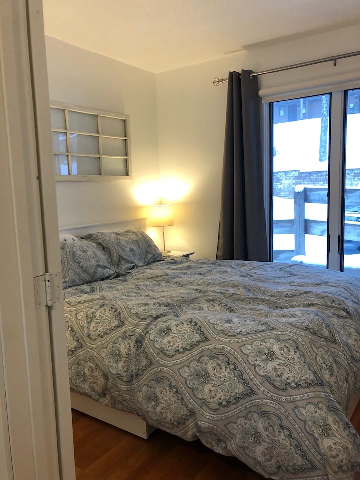 Dormitorio en el segundo piso con gran ventana. Cama tamaño queen con cubrecamas de plumas, tocador, 2 mesitas de noche y armario.