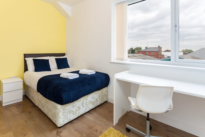 Wake up in a bright and airy bedroom with a comfortable double bed, luxurious bedding, and a dedicated workspace. The vibrant yellow walls energize the room, making it a cheerful space to start your day.