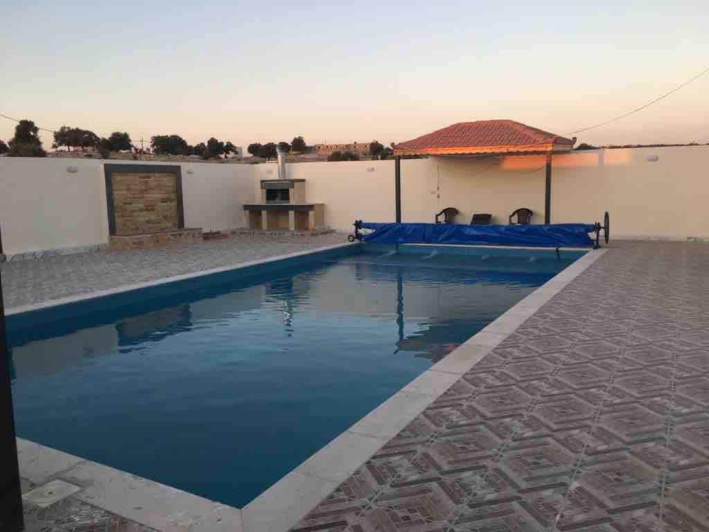 A private pool is depicted, surrounded by a tiled deck and a BBQ pit shaded by a roof. Sun loungers are positioned nearby, and the serene sky reflects a soft dusk light. The space is enclosed by a low wall, enhancing privacy.
