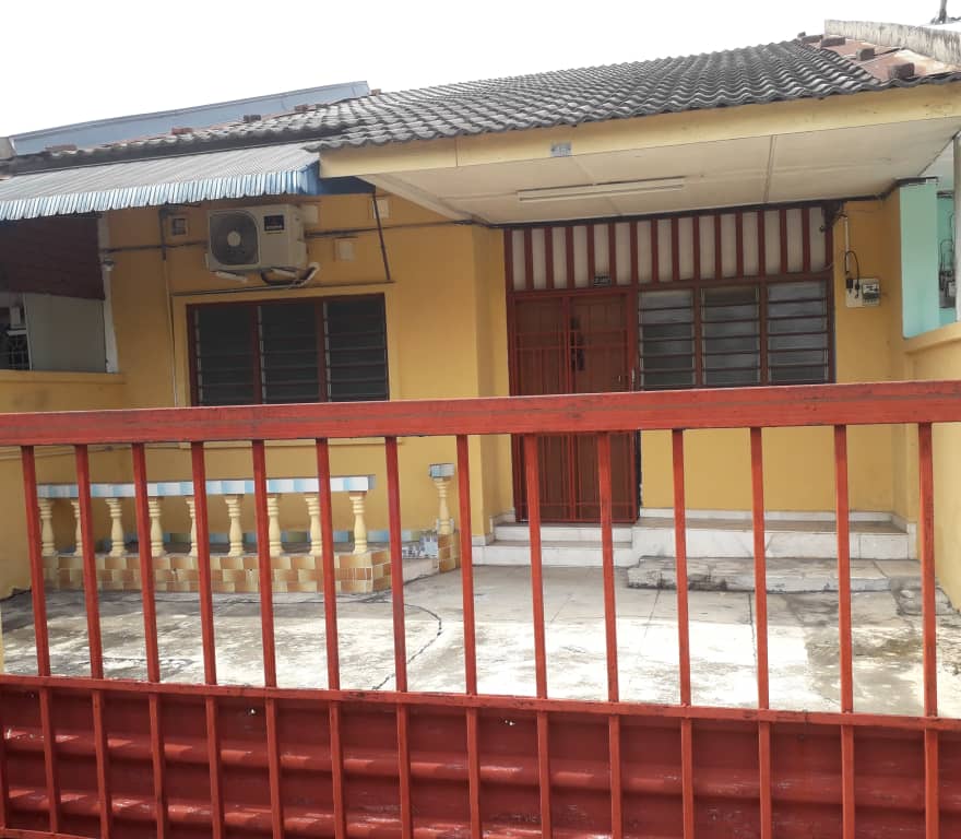 A single-story building showcases a bright yellow exterior, framed by a red railing. Large windows allow light into the interior space, while a simple entrance door is centered at the front, partially sheltered by an overhang. The surrounding area is paved with concrete.