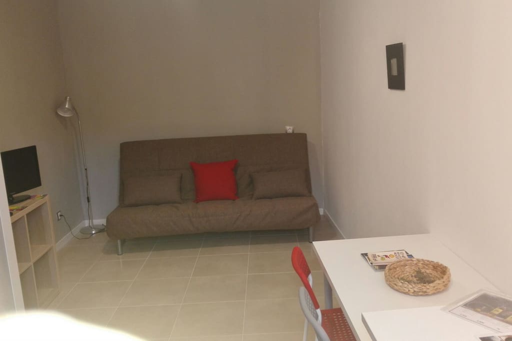 sofa llit. moble amb tv. taula i cadires.
