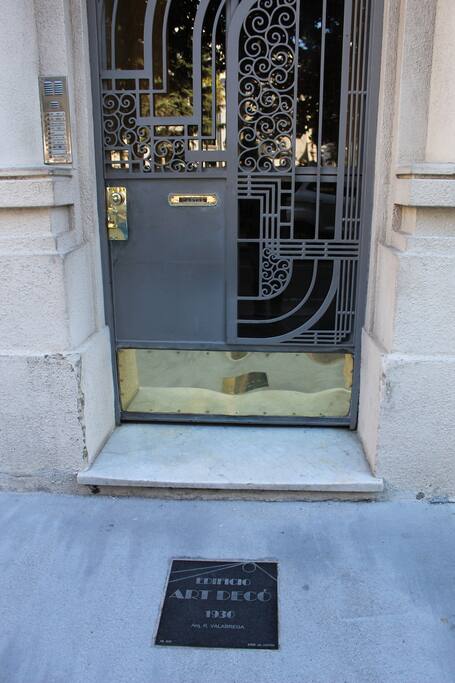 Puerta de entrada al edificio, con placa recordatoria en la acera.