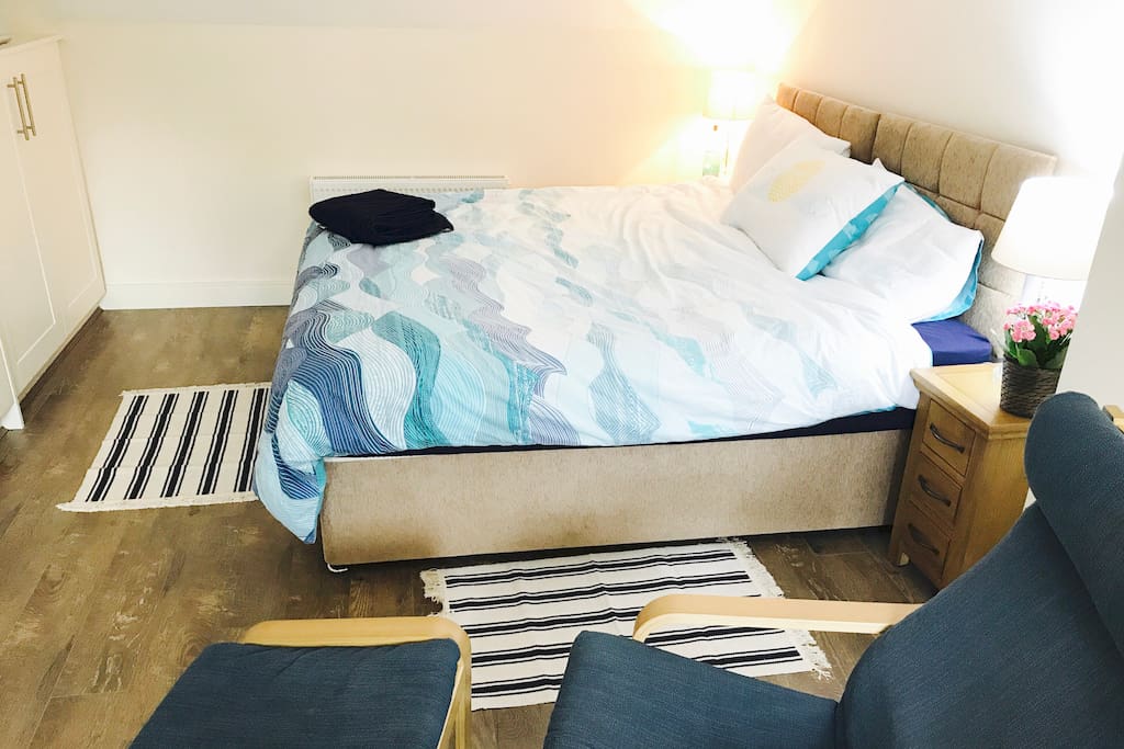 One half of large bedroom with two single beds pushed together. Each side has its own bedside table. Lots of surface space and seating out of view.