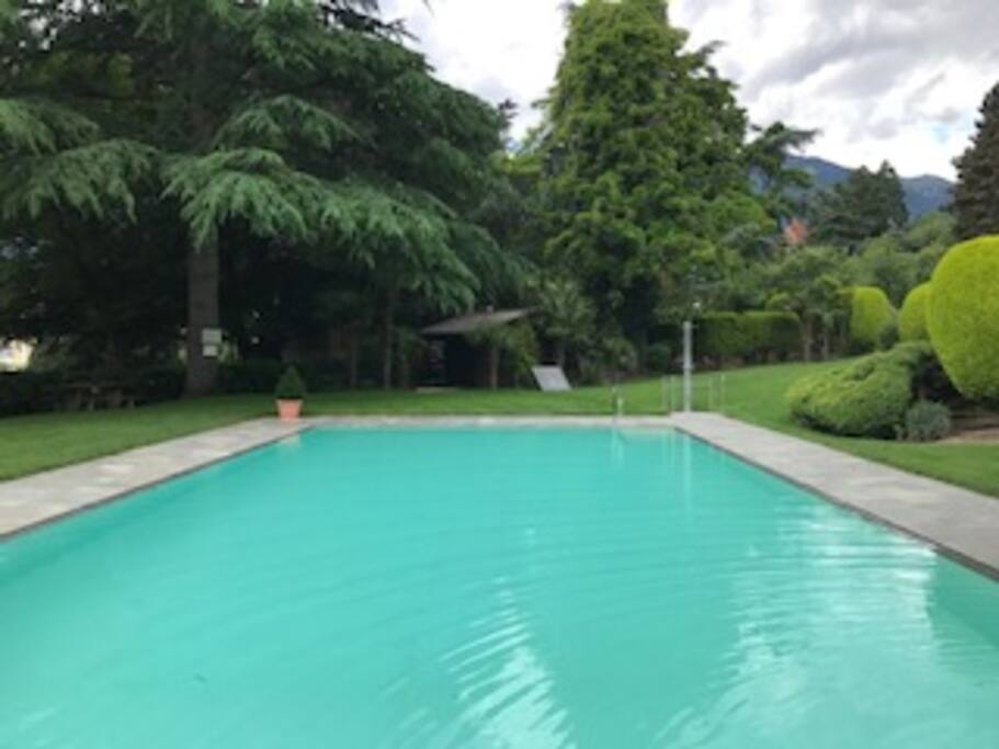 Großer beheizter Pool mit Gartendusche und Poolliegen in parkähnlichen Garten mit Blick auf Meran und die umliegenden Berge