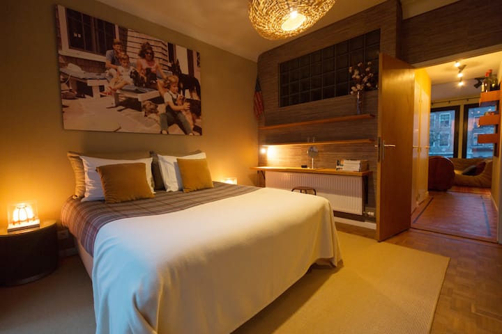 غرفة نوم هادئة بإضاءة خافتة وأعمال فنية فوق السرير وأجواء هادئة وجذابة