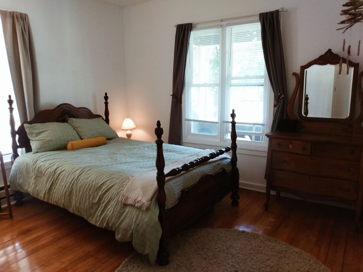 ห้องนอนมีเตียงควีนไซส์เฟอร์นิเจอร์ไม้สไตล์วินเทจและผ้าม่านสีเข้ม 