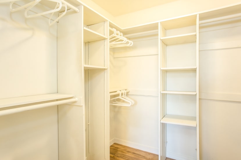 An organized and airy closet space is presented, featuring multiple hanging rods and shelving units. The white walls and light-colored flooring create a bright environment, allowing for ample storage options for personal items and clothing.