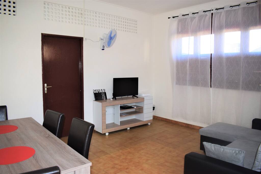 Séjour lumineux et équipé d'une tv, ventilateur mural, table à manger et canapé d'angle convertible