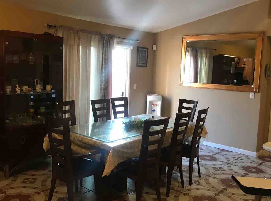 A couple steps in and you see the 8 person dinning table made out of Italian wood, covered with table clothes. On side wall there's a 70” glass mirror. Also sliding door to backyard.
