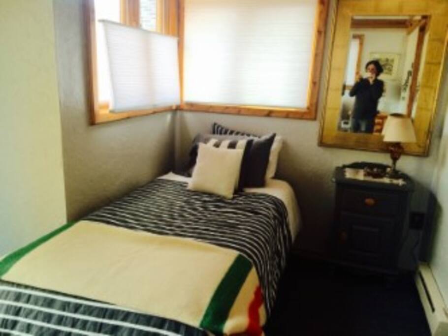 East twin bed with luxury linens and lots of windows for taking in the scenery and cross ventilation. There is a ceiling fan.