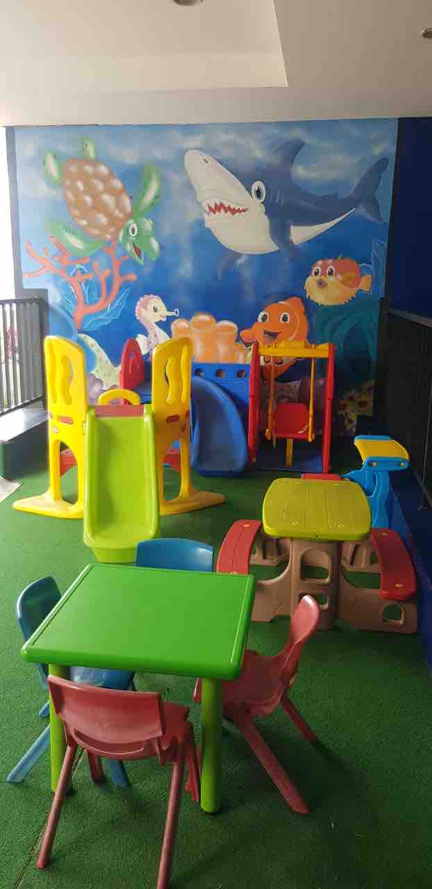 A vibrant play area is filled with colorful playground equipment, including slides and climbing structures. Brightly colored tables and chairs are arranged for children. A cheerful mural depicting sea creatures adorns the wall, creating a lively atmosphere for young guests.