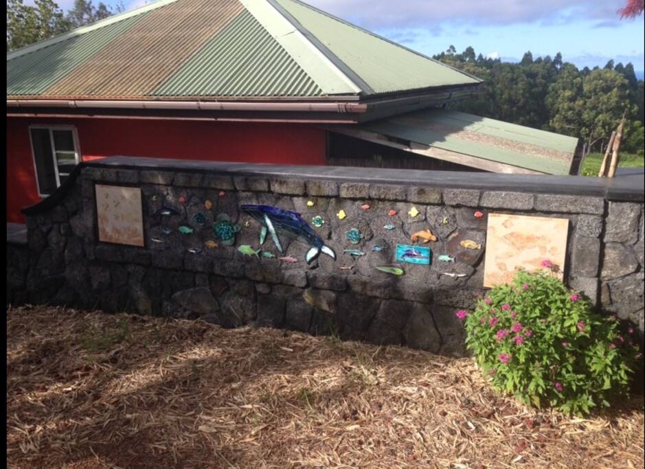 Tongan-built rock wall with whales, dolphins, and other ocean life greets guests by parking area.