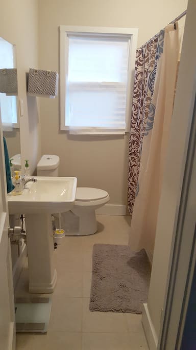 Private, full-size bathroom with large tub, pedastal sink, and storage shelft