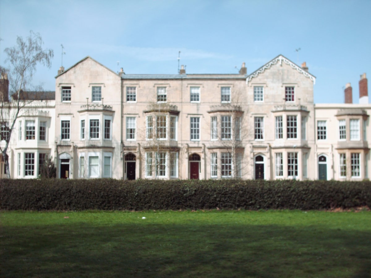 A row of elegant Georgian-style homes is displayed, featuring large windows and distinct architectural details. The buildings are framed by manicured green grass in the foreground, enhancing the appealing view of the neighborhood.