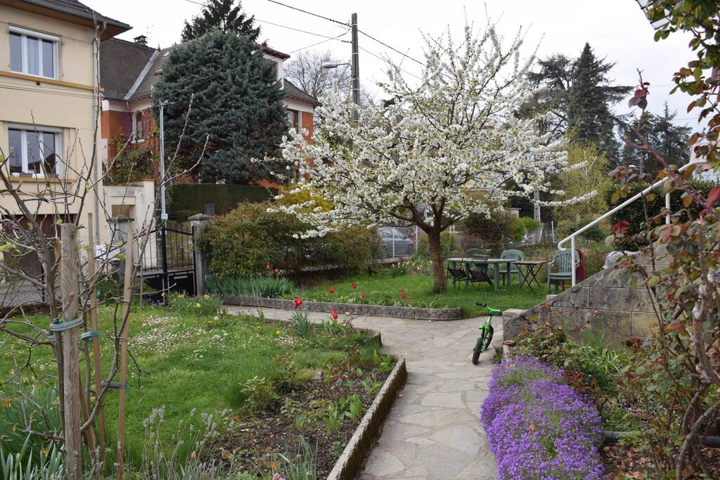 Jardin et espace détente sous le cerisier avec barbecue, balançoire et bac à sable.