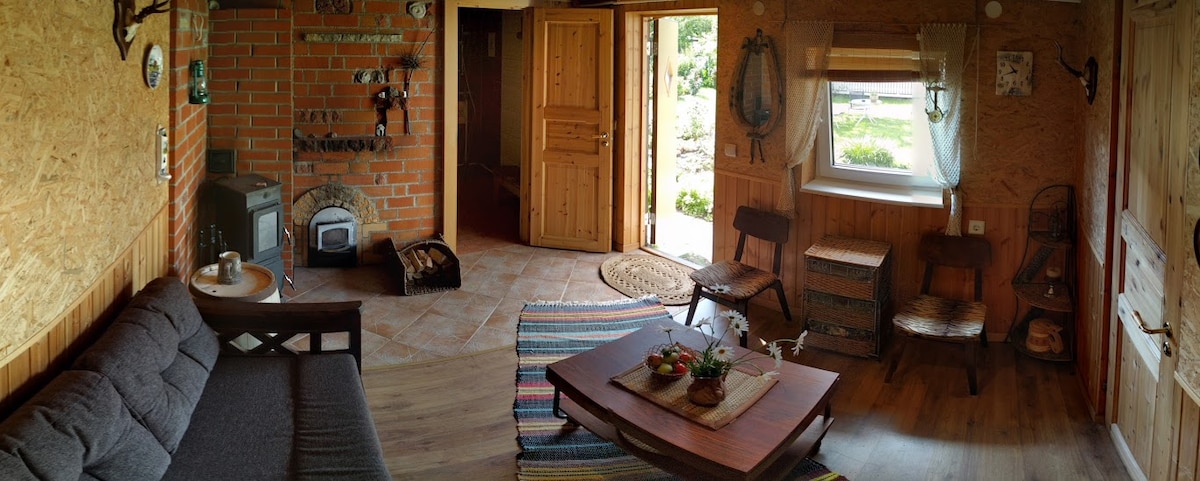 A welcoming living space is shown, featuring a wooden door that opens to the outside. A cozy sofa sits beside a low coffee table, which is set with snacks. An area rug adds warmth to the wooden floor, and natural light is welcomed through the nearby window.